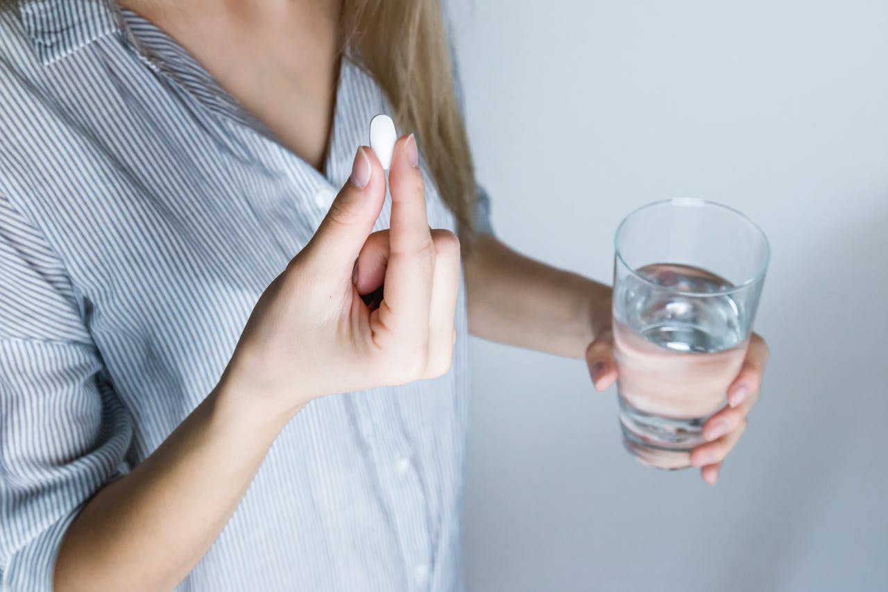 services-04 Close-up of a woman holding a pill and a glass of water, ready to take medication.